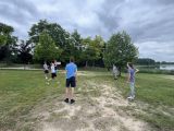 Na plaży przy jezierze siecioro uczniów liceum odbija piłkę do siatkówki.