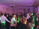 Grupa kilkudziesięciu nastolatków,  tańczących w strojach wieczorowych.