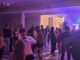Grupa kilkudziesięciu nastolatków, tańczących w strojach wieczorowych.