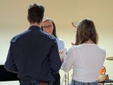 Dwoje gimnazjalistów stojących tyłem. Przed nimi uśmiechnięta kobieta w okularach