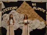 Dwie nastolatki w białych strojach. W tle dekoracja z napisem Otrzęsiny na Olimpie