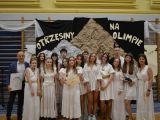 Grupa nastolatków, z kobietą i mężczyzną na bokach . W tle napis Otrzęsiny na Olimpie